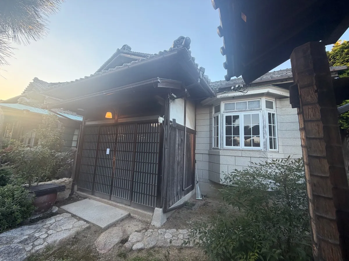 格子戸の和風玄関の隣に、白い窓枠の洋風出窓が並ぶ和洋折衷の外観。夕暮れの光